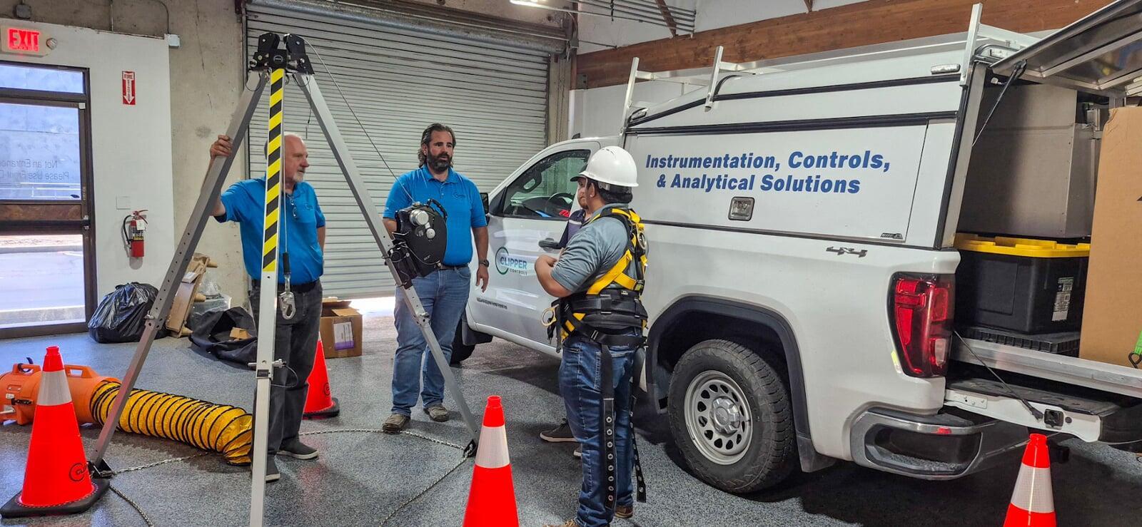 Clipper Controls technicians preparing for confined space entry training with tripod retrieval equipment and service truck