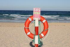Orange life preserver hanging from a post containing a SOS sign on an ocean beach with medium size waves curling in the background