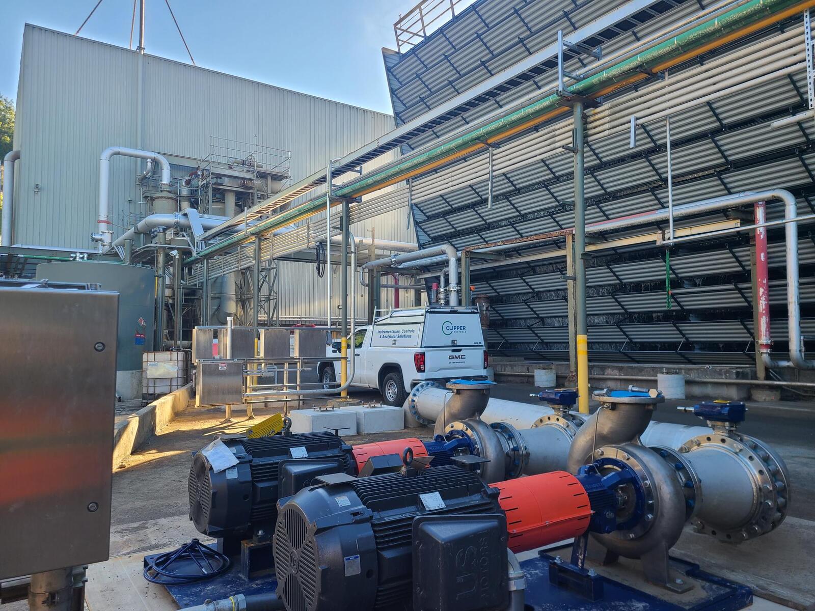 Clipper Controls branded truck at an industrial facility by large pumps and a colling tower